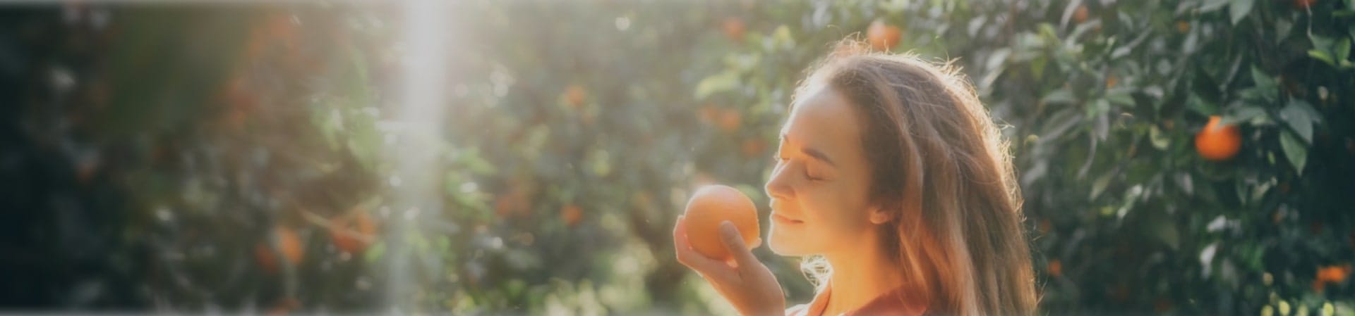 a woman smelling an orange in an orange grove - IFF Taste's citrus flavor solutions