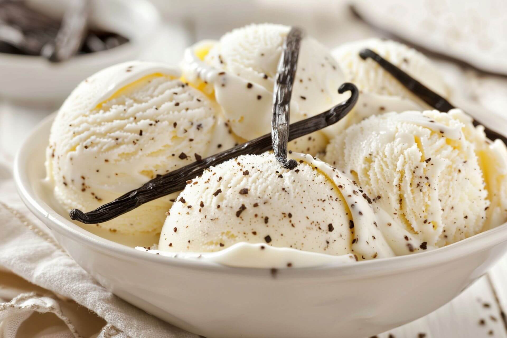 Vanilla bean ice cream in a white bowl with vanilla beans on top and in the background.