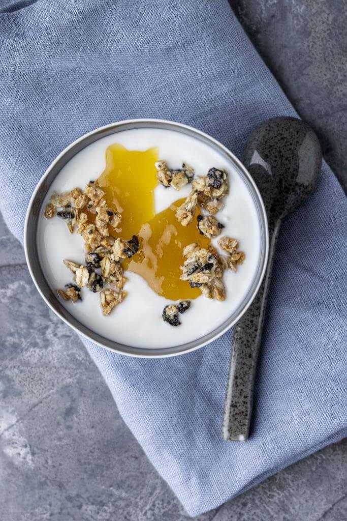 Plant Base Bowl of yogurt topped with granola and honey, placed on a blue cloth with a spoon beside it