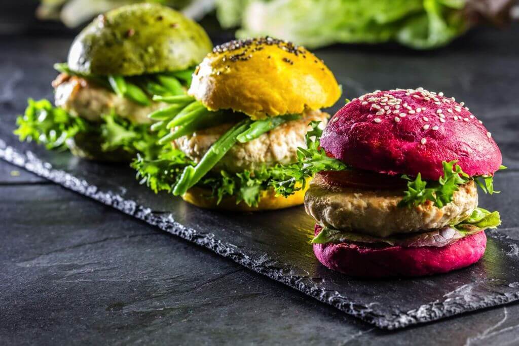 Three delicious, plant-based burgers made with IFF pea protein in colorful buns displayed on black slate
