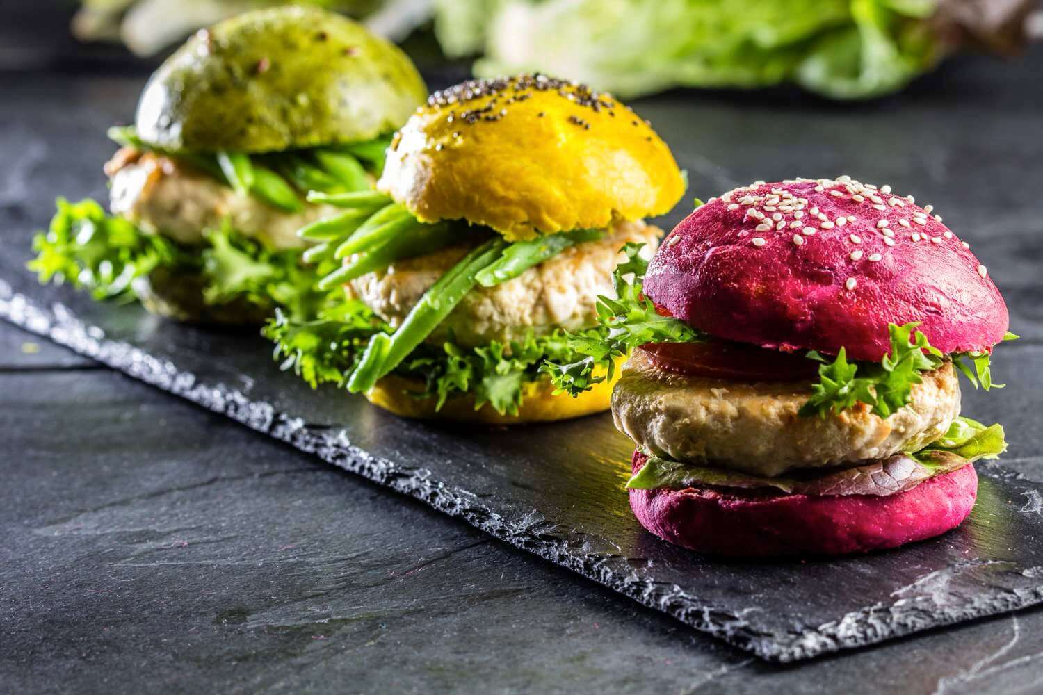 Three delicious, plant-based burgers made with IFF pea protein in colorful buns displayed on black slate