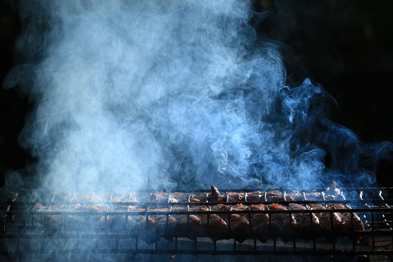 Smoke rising from meat, coming up from a grill. Pitch-black background
