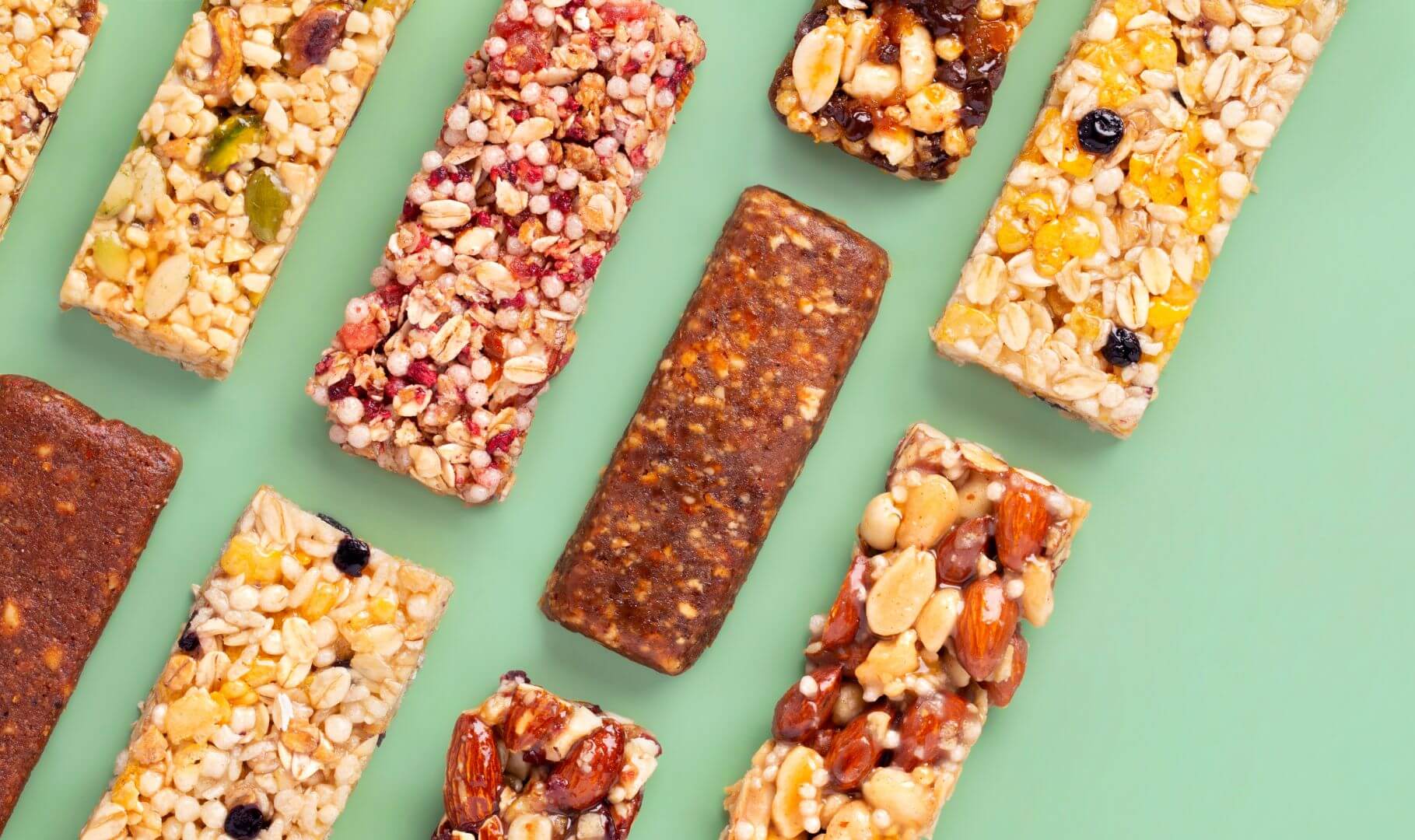 Multiple types of snack bars of different varieties and colors sitting next to each other in diagonal rows, all set against a bright green background
